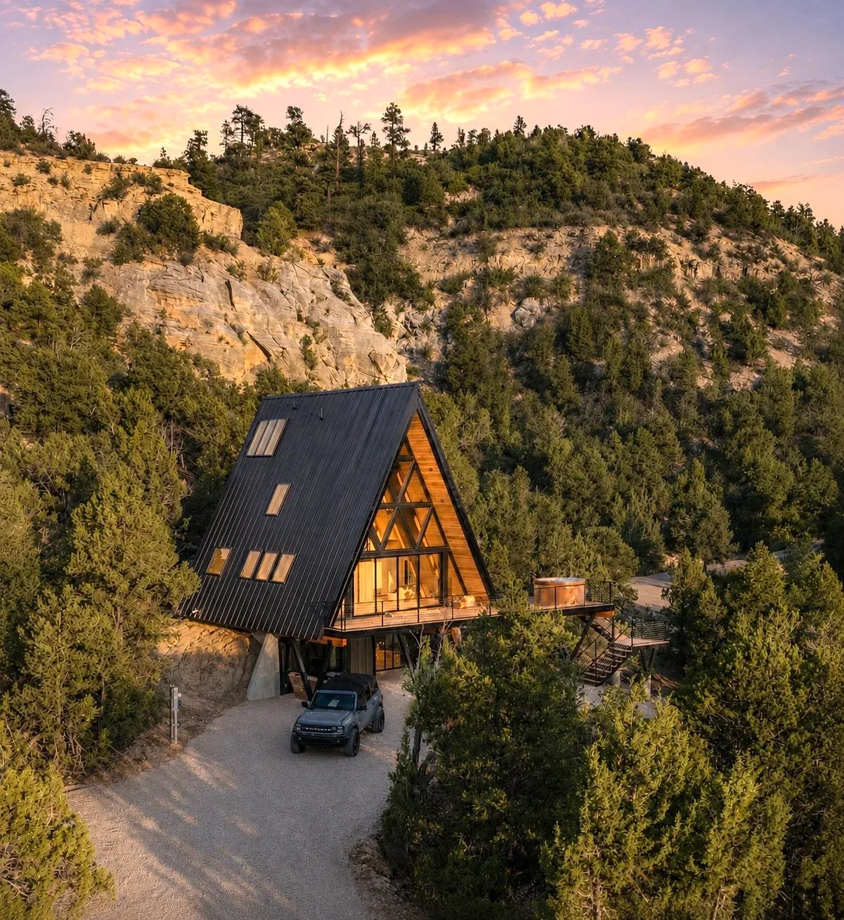 Arka from above at sunset: the A-frame on a wooded hillside below pale limestone cliffs, the sky going gold.