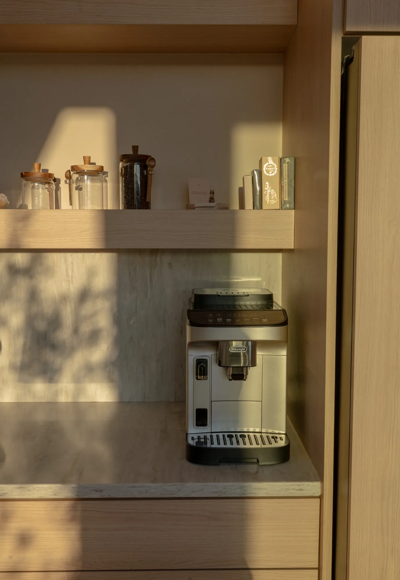 The espresso machine on a pale stone counter in a niche of open wooden shelves.